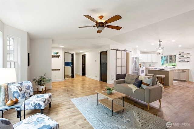 living area featuring a barn door, healthy amount of natural light, light wood-style flooring, baseboards, and vaulted ceiling