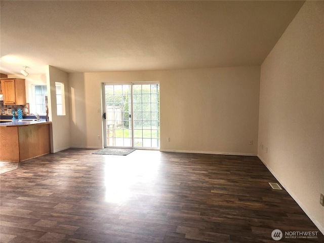 unfurnished living room featuring dark wood-style flooring, visible vents, baseboards, and a sink