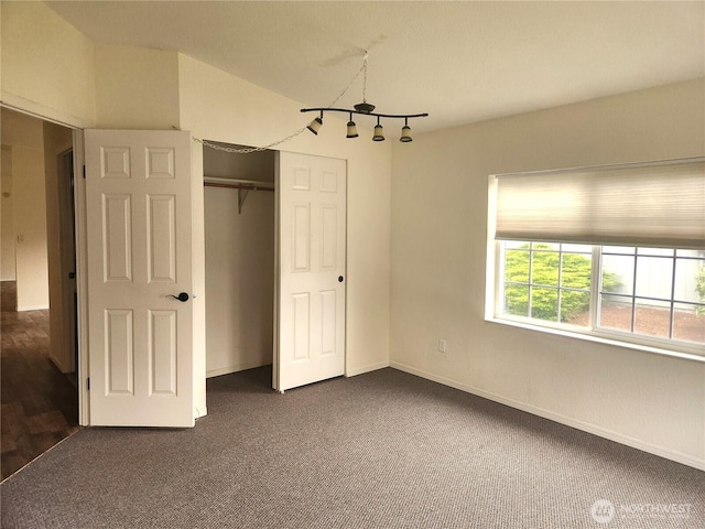 unfurnished bedroom with a closet, dark colored carpet, and baseboards