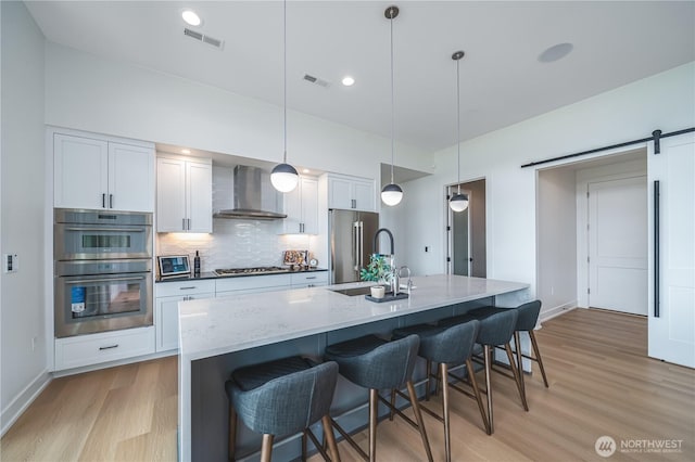 kitchen with wall chimney range hood, tasteful backsplash, appliances with stainless steel finishes, and visible vents