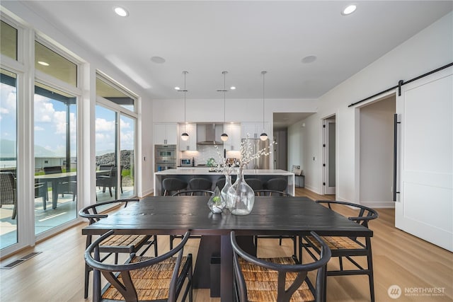 dining area featuring a barn door, light wood-type flooring, baseboards, visible vents, and recessed lighting