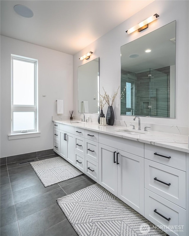 full bathroom with double vanity, a sink, a stall shower, and baseboards