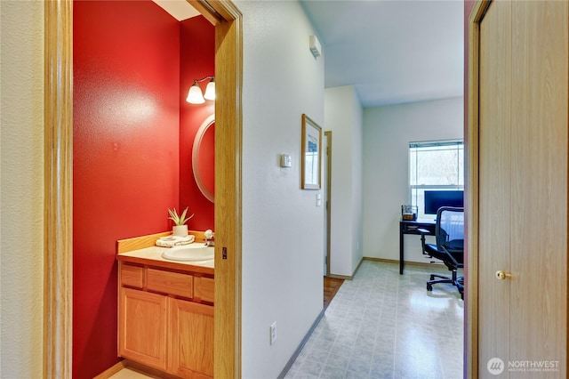 hall featuring a sink, baseboards, and light floors