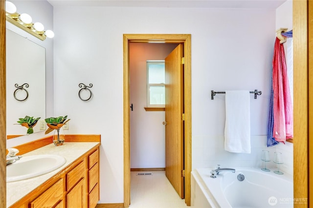 bathroom with visible vents, baseboards, vanity, and a garden tub