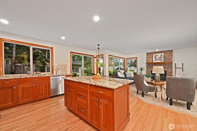 kitchen with light wood-style flooring, stainless steel dishwasher, light stone counters, a sink, and brown cabinets