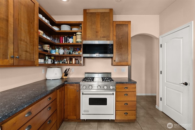 kitchen with open shelves, stainless steel microwave, light tile patterned flooring, white range with gas stovetop, and brown cabinetry