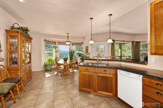 kitchen with a sink, dishwasher, hanging light fixtures, brown cabinetry, and dark stone counters