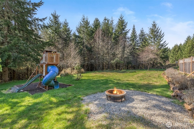 view of yard featuring a playground, a fire pit, fence, and a view of trees