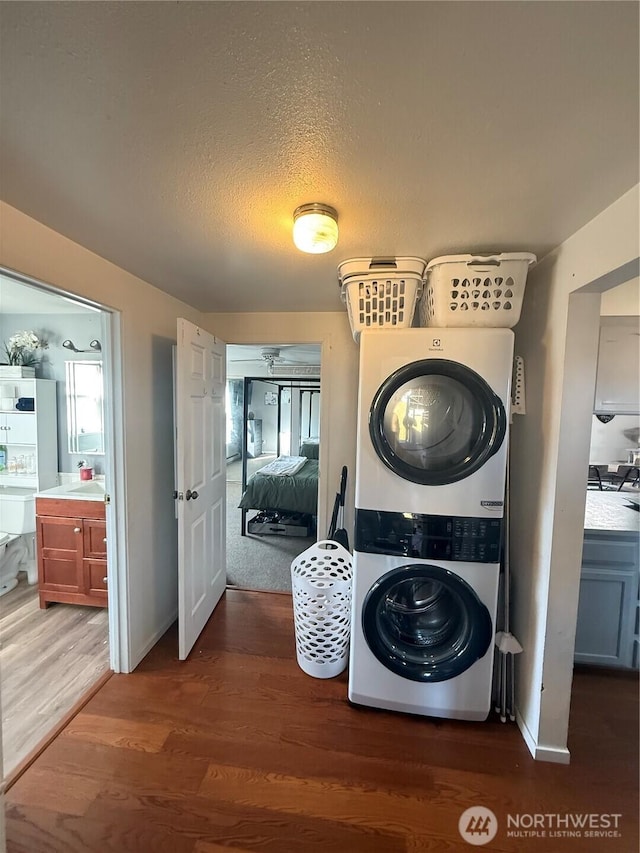 clothes washing area with stacked washer and dryer, a textured ceiling, laundry area, and wood finished floors