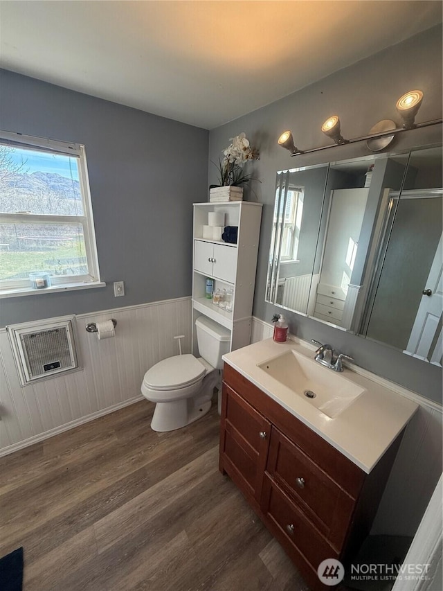 bathroom with a wainscoted wall, heating unit, toilet, vanity, and wood finished floors