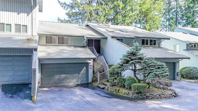 view of front of property with driveway, an attached garage, stairway, and roof with shingles