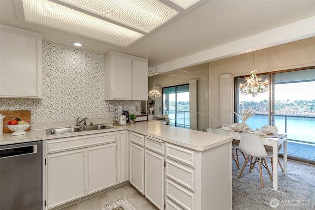 kitchen with a notable chandelier, light countertops, a sink, a peninsula, and stainless steel dishwasher
