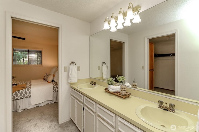 bathroom with ensuite bathroom, double vanity, a textured ceiling, and a sink