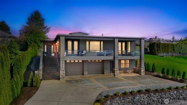 rear view of property with concrete driveway, stairs, an attached garage, stone siding, and a balcony