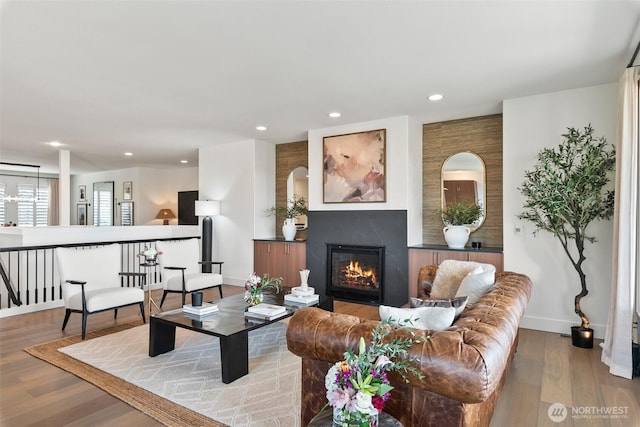 living area with baseboards, wood finished floors, a glass covered fireplace, and recessed lighting