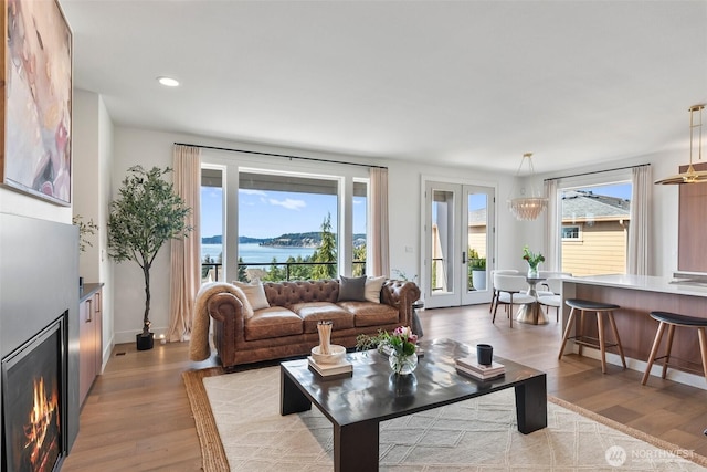 living room with light wood-style flooring, recessed lighting, a water view, baseboards, and a warm lit fireplace
