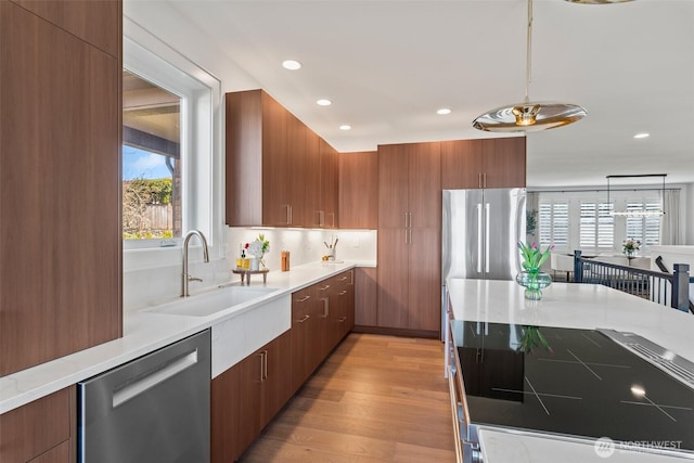 kitchen with light wood-style flooring, modern cabinets, appliances with stainless steel finishes, a sink, and hanging light fixtures