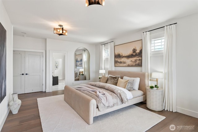 bedroom featuring baseboards, arched walkways, and wood finished floors