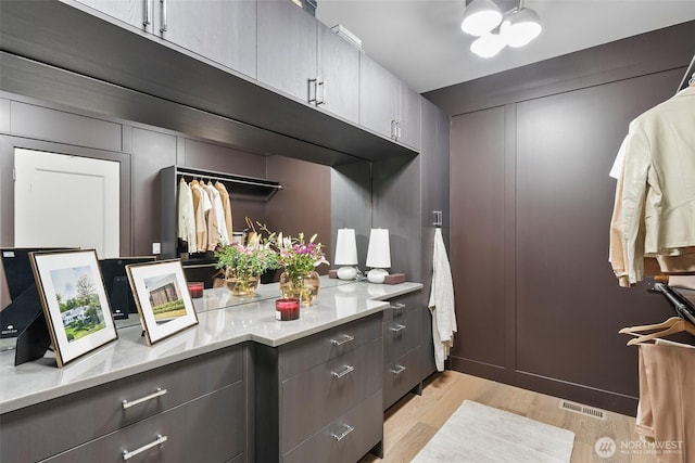 walk in closet with light wood-type flooring, an inviting chandelier, and visible vents
