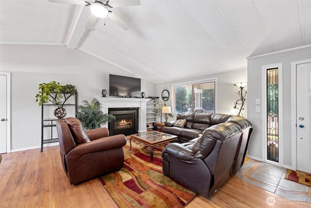 living area with lofted ceiling with beams, light wood finished floors, baseboards, a ceiling fan, and a glass covered fireplace