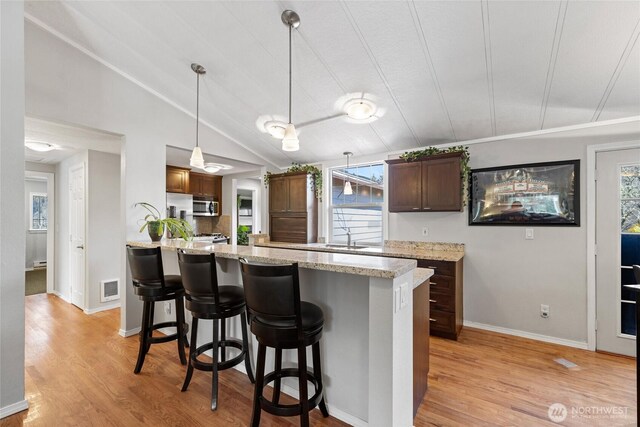 kitchen with visible vents, light wood-style flooring, stainless steel microwave, lofted ceiling, and a sink