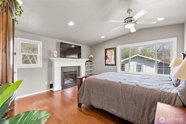 bedroom featuring a tiled fireplace, wood finished floors, lofted ceiling, baseboards, and recessed lighting