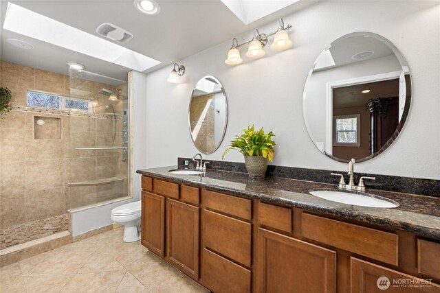 bathroom with toilet, a sink, a skylight, and a tile shower