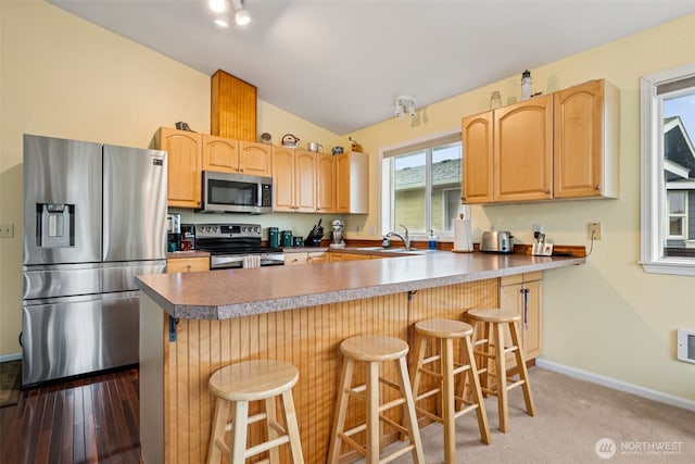kitchen with a sink, vaulted ceiling, light brown cabinetry, and appliances with stainless steel finishes