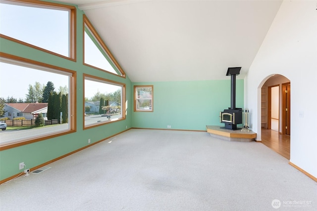 305 W Eunice St, Sequim, WA 98382 - unfurnished living room featuring arched walkways, high vaulted ceiling, a wood stove, and carpet floors