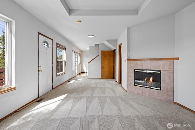 unfurnished living room featuring stairway, light carpet, a fireplace, baseboards, and visible vents