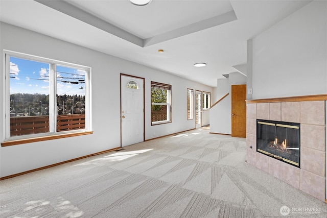 unfurnished living room featuring a tile fireplace, baseboards, and light carpet