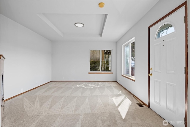 entrance foyer with light colored carpet, baseboards, a tray ceiling, and visible vents