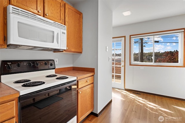 kitchen featuring electric stove, light wood finished floors, light countertops, white microwave, and baseboards