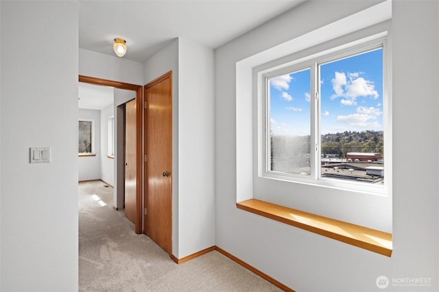 hallway with baseboards and light colored carpet
