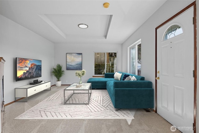 carpeted living area featuring a raised ceiling and baseboards