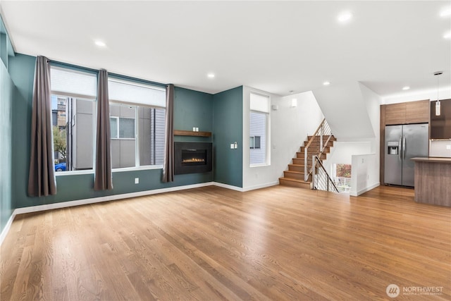 2620 SW Nevada St, Seattle, WA 98126 - unfurnished living room with a warm lit fireplace, baseboards, stairway, and light wood-style floors