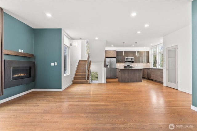 2620 SW Nevada St, Seattle, WA 98126 - unfurnished living room with baseboards, light wood-style floors, recessed lighting, stairway, and a glass covered fireplace