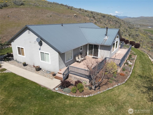 rear view of property featuring a deck with mountain view, a lawn, and metal roof