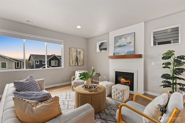 living room featuring recessed lighting, wood finished floors, visible vents, baseboards, and a glass covered fireplace