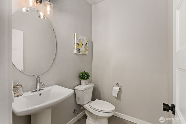 half bathroom with baseboards, a sink, and toilet