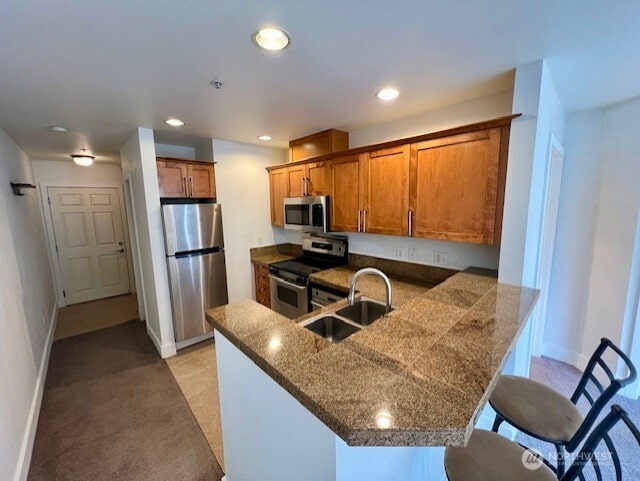 123 Queen Anne Ave N Unit 405, Seattle, WA 98109 - kitchen featuring a peninsula, a breakfast bar, a sink, stainless steel appliances, and brown cabinetry