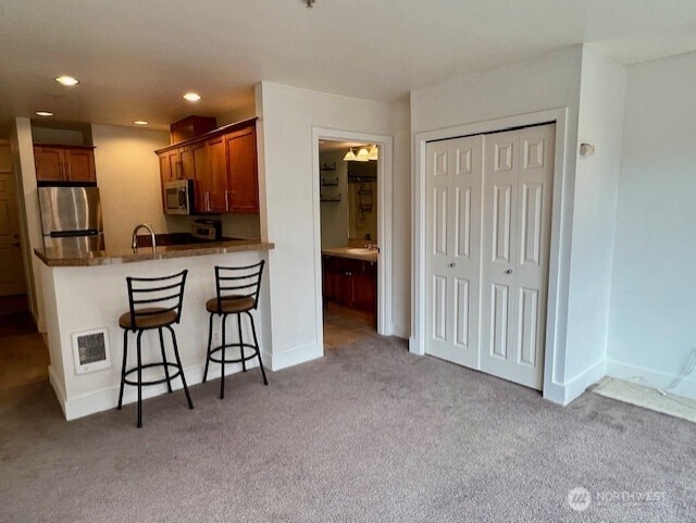 123 Queen Anne Ave N Unit 405, Seattle, WA 98109 - kitchen with a peninsula, stainless steel appliances, brown cabinetry, light colored carpet, and a breakfast bar area