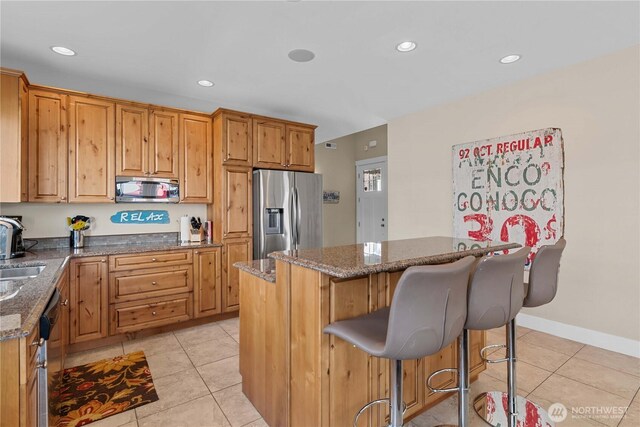 kitchen with a kitchen island, light tile patterned flooring, appliances with stainless steel finishes, and dark stone counters