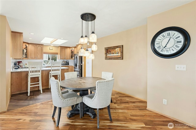 dining room featuring baseboards, recessed lighting, a skylight, and light wood finished floors