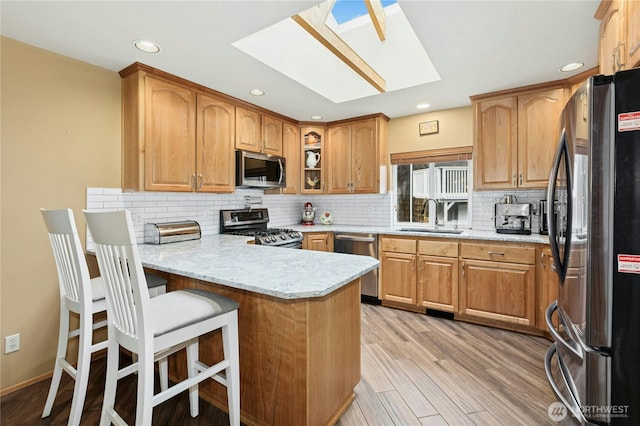 kitchen with a skylight, a peninsula, stainless steel appliances, a sink, and light wood-style floors