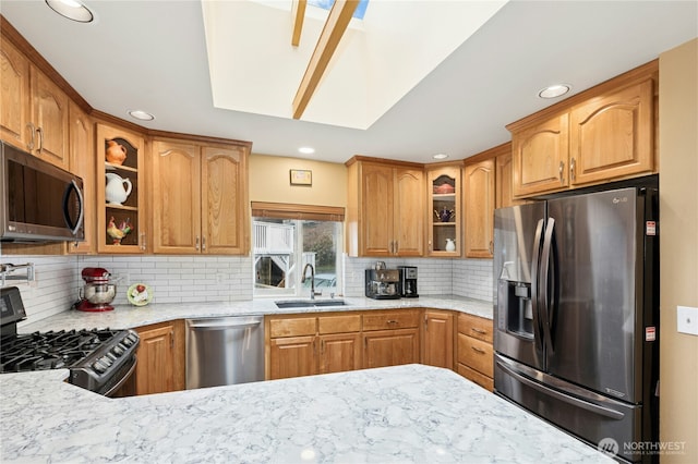 kitchen with tasteful backsplash, stainless steel appliances, a sink, light stone counters, and glass insert cabinets
