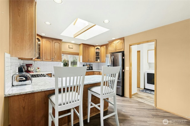 kitchen featuring a kitchen breakfast bar, stainless steel fridge, a skylight, a peninsula, and glass insert cabinets