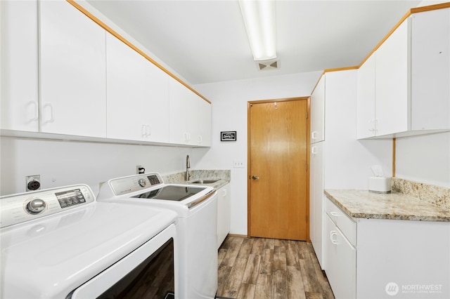 washroom featuring light wood-type flooring, cabinet space, a sink, and washer and dryer