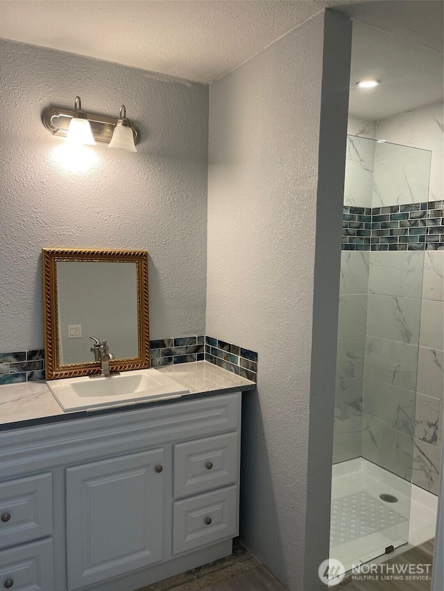 full bathroom featuring a tile shower, a textured wall, and vanity