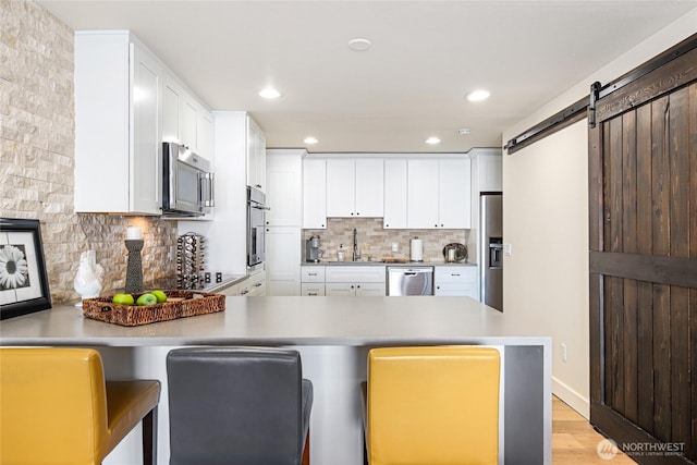 kitchen with decorative backsplash, white cabinets, a peninsula, appliances with stainless steel finishes, and light wood-type flooring